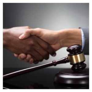 A photo of two adult hands in a handshake with a gavel in the foreground.